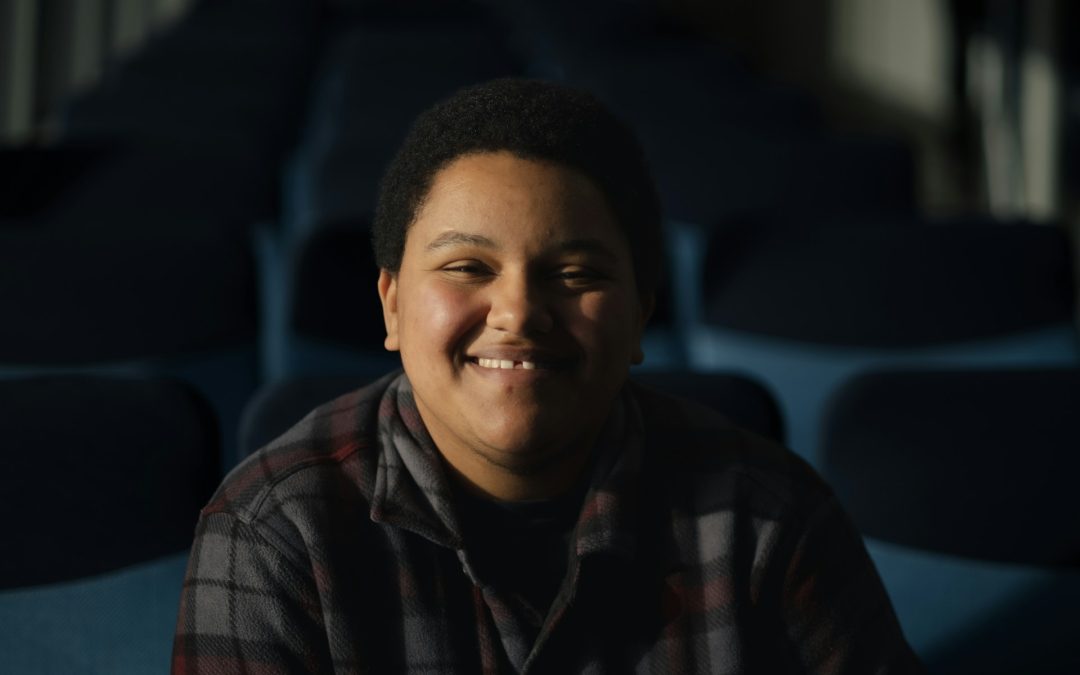 Smiling young individual in a checked shirt seated in a dental office, representing the welcoming atmosphere of Oro Valley Dental Arts for cosmetic dentistry consultations.